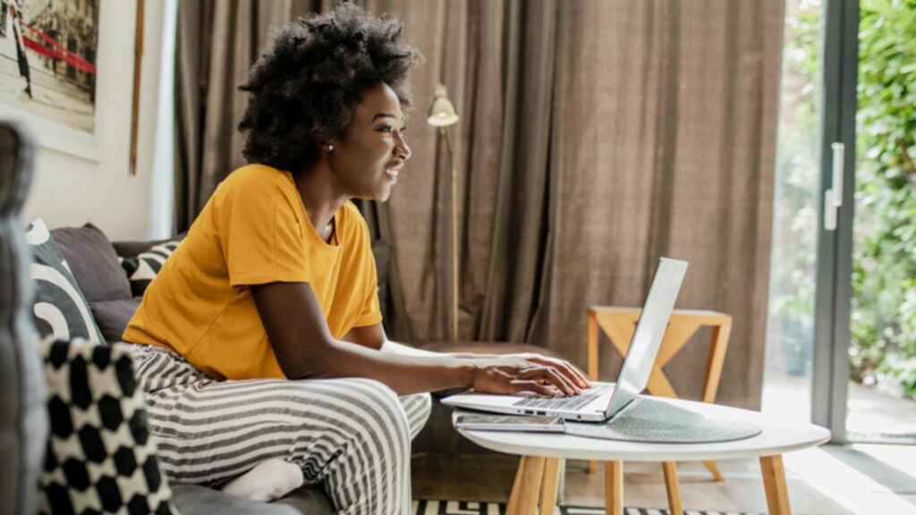 a lady wearing a yellow top looking at a laptop smiling reading about the most common apartment fees 
